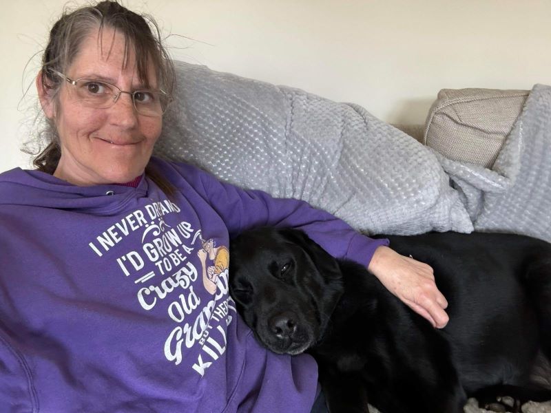Sarah and a black lab cuddling on a sofa.