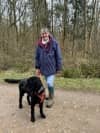 Sarah and a black Goldendoodle dog standing on a path in the woods
